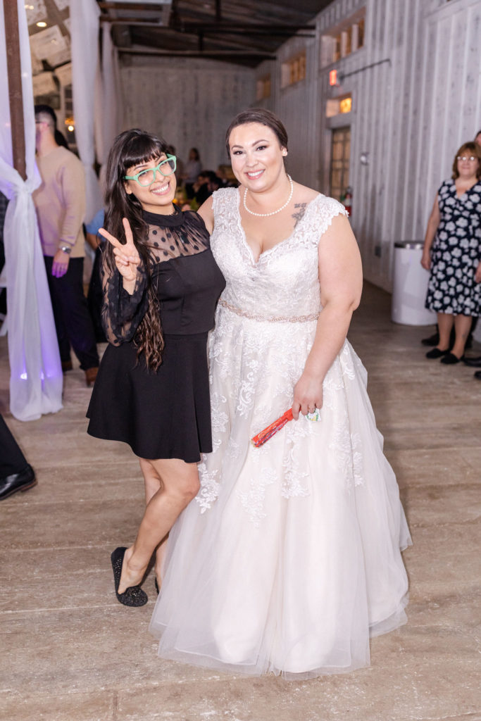 Bride at wedding reception with wedding guest wearing black dress and green glasses