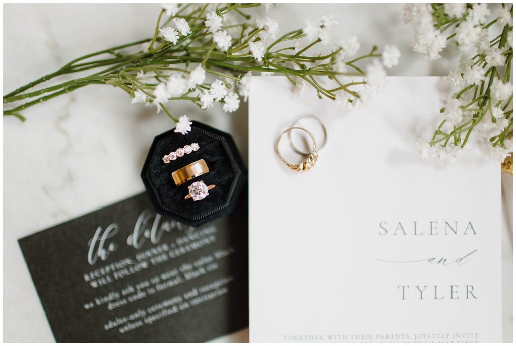 wedding flat lay details including wedding rings in a black velvet octagon ring box and black and white wedding invitations