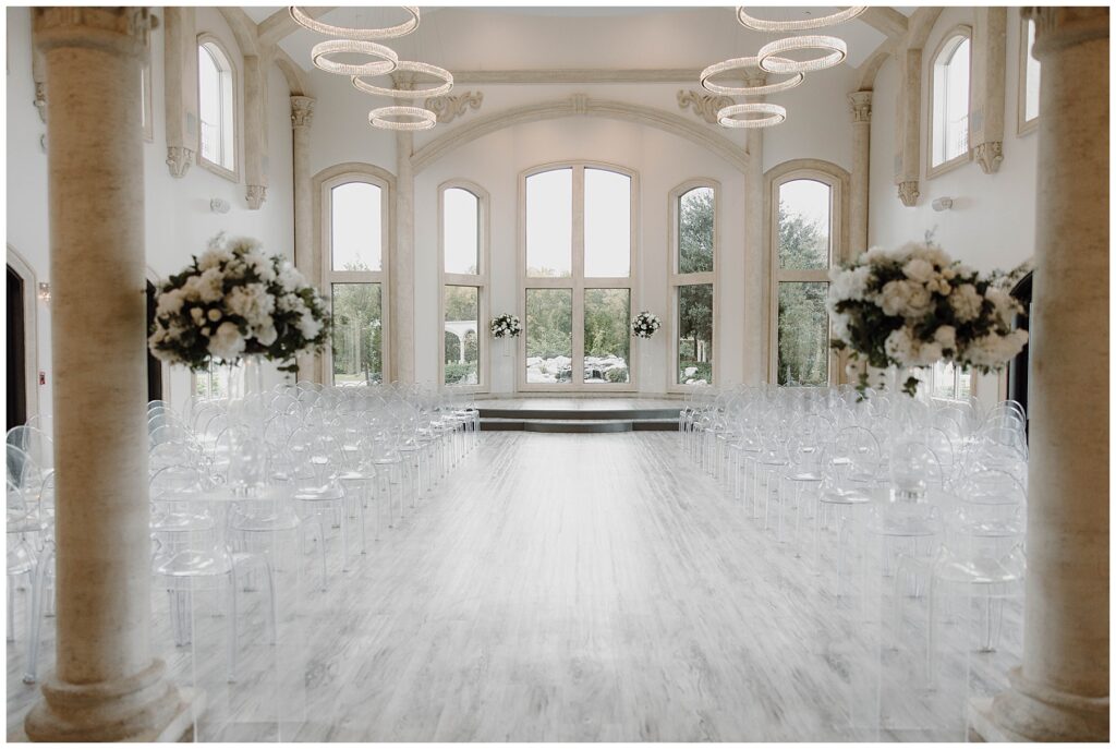 Wedding ceremony space at Knotting Hill Place with large windows, clear acrylic chairs, and flower installations on clear pedestals. 