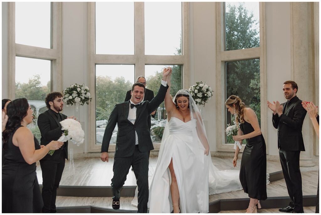 Bride and groom cheering and raising joined hands as they begin the recessional 