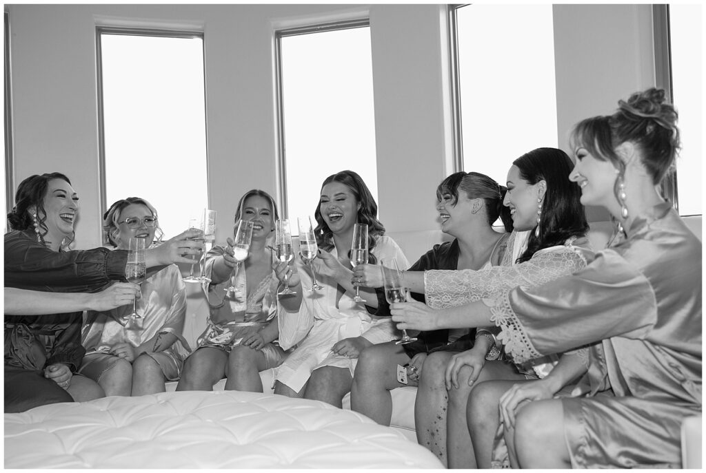 Bride and bridesmaids wearing robes and clinking champagne glasses while getting ready for the wedding at Knotting Hill Place