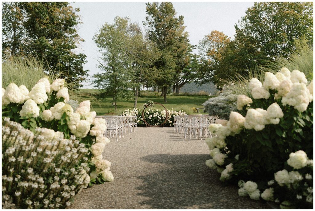 outdoor wedding ceremony space with white chairs, a circular wedding arbor, and white hydrangea bushes