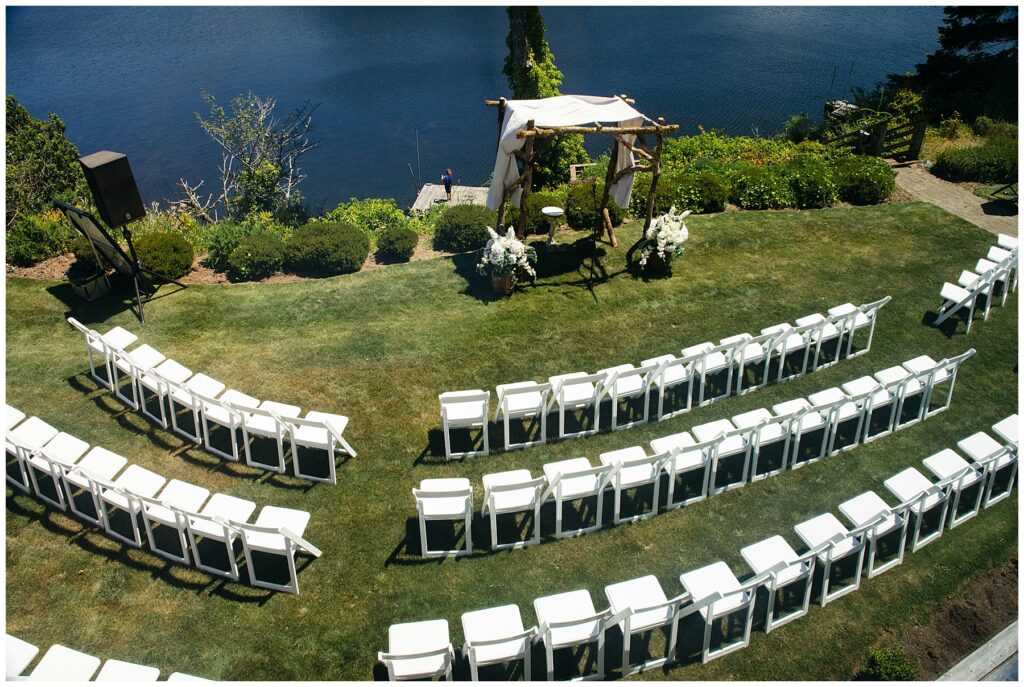 wedding ceremony space with white chairs arranged in three sections creating two aisles with water in background