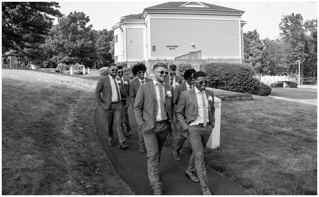 groomsmen wearing suits walking down paved path with Founders Hall in the background
