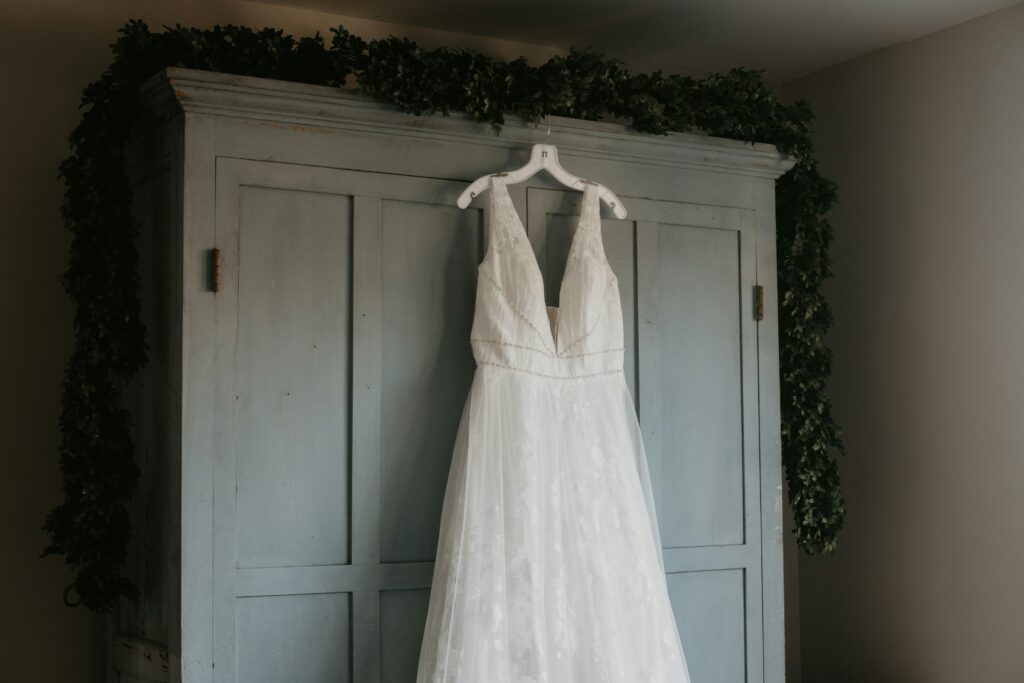 v neck wedding gown hanging on white hanger from a blue wooden armoir