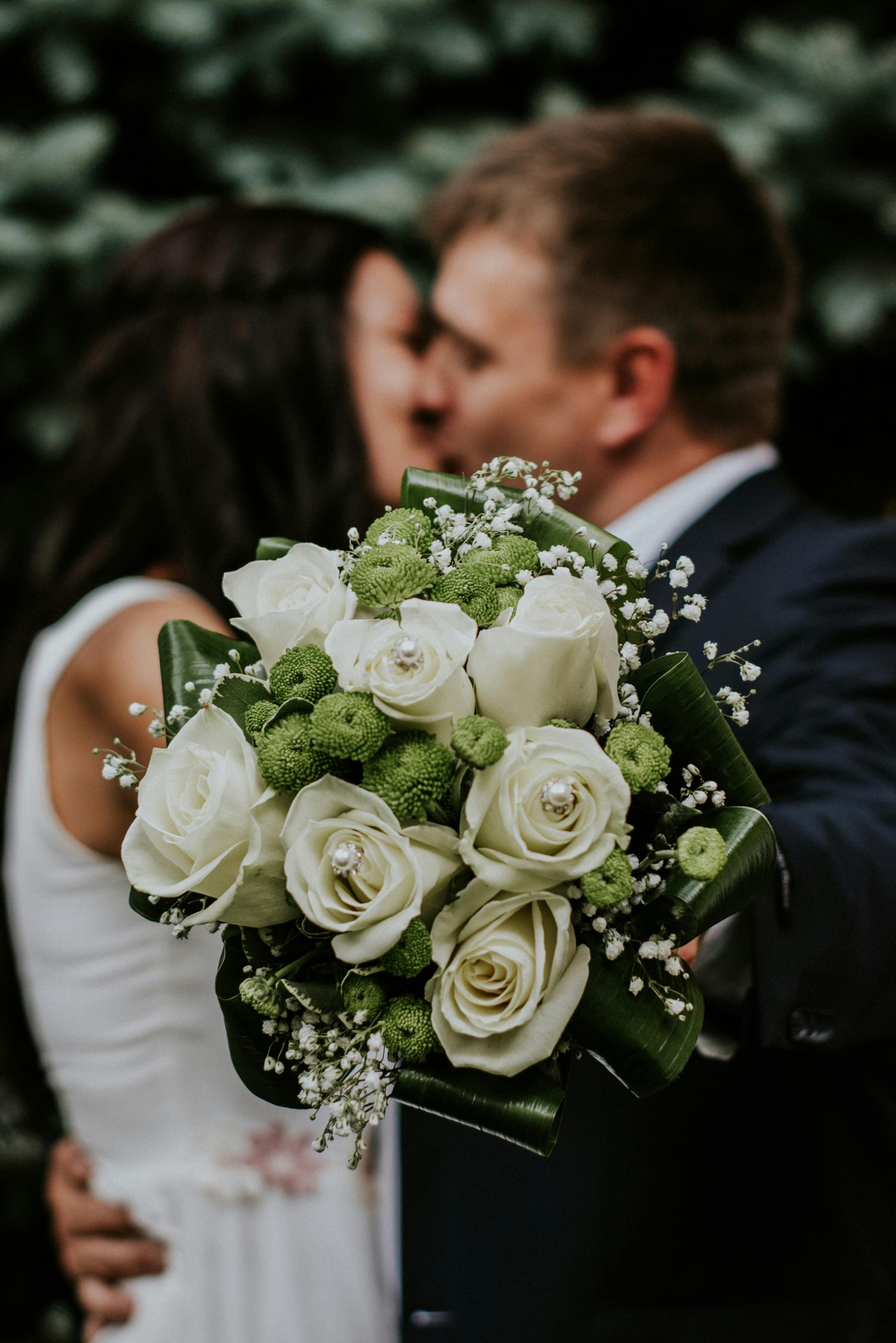 Bride and groom kissing behind a bouquet of white roses and green chrysanthemums